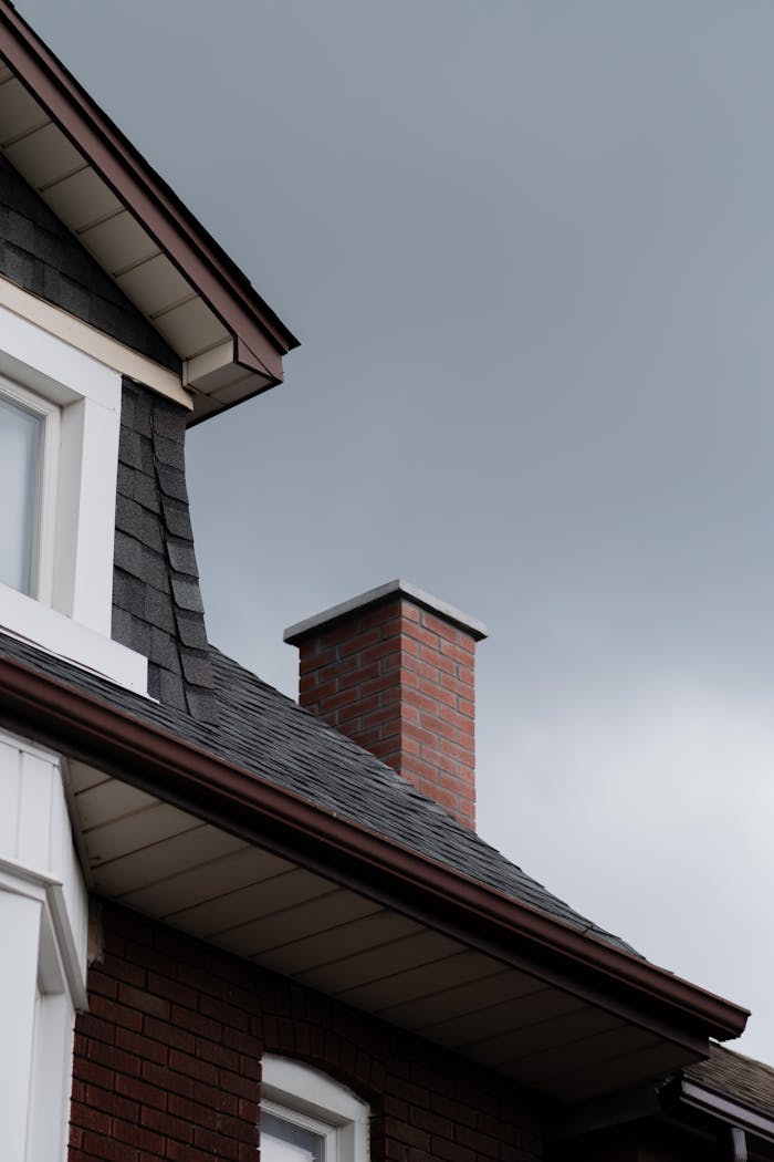 Close-up of a house roof with a brick chimney against a cloudy sky.