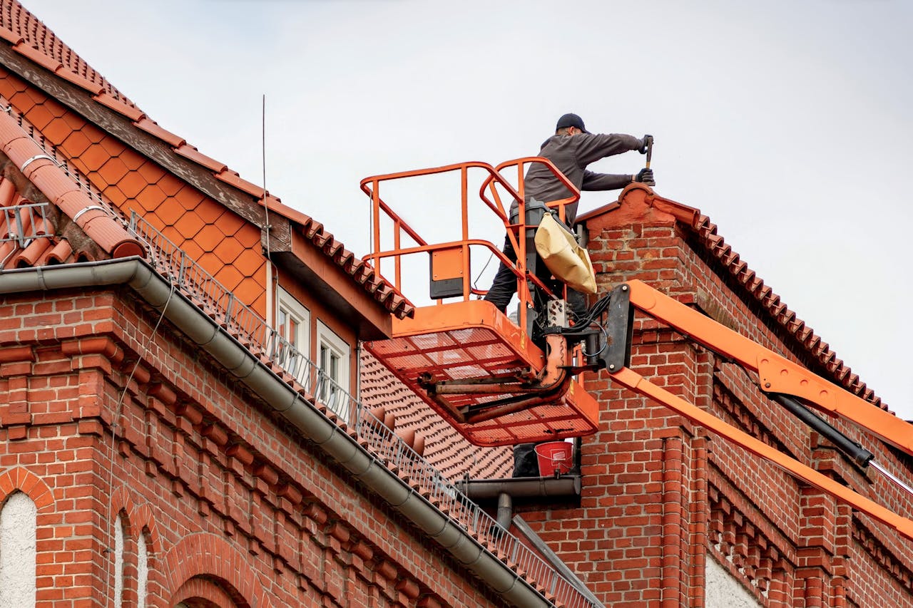 services-05 Roofer in a cherry picker conducting maintenance on a red brick building with a tiled roof.